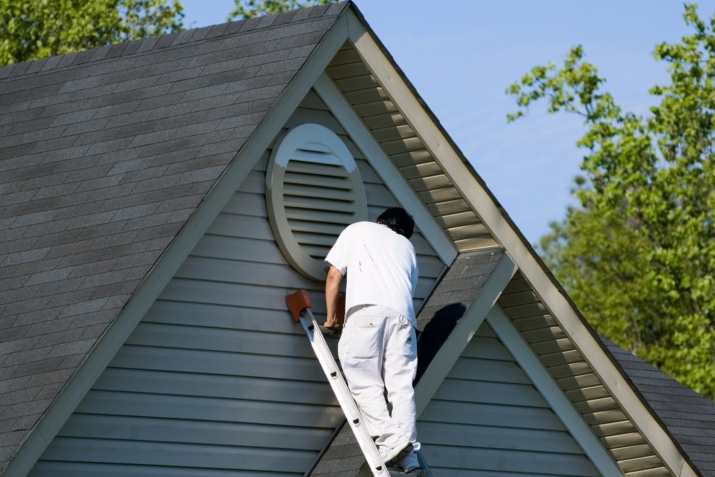 Painter working from an extension ladder on a two-story home